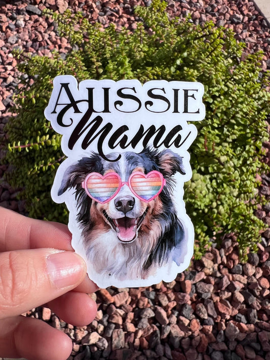 Sticker with a dog's face and 'Aussie Mama' text held over a natural background